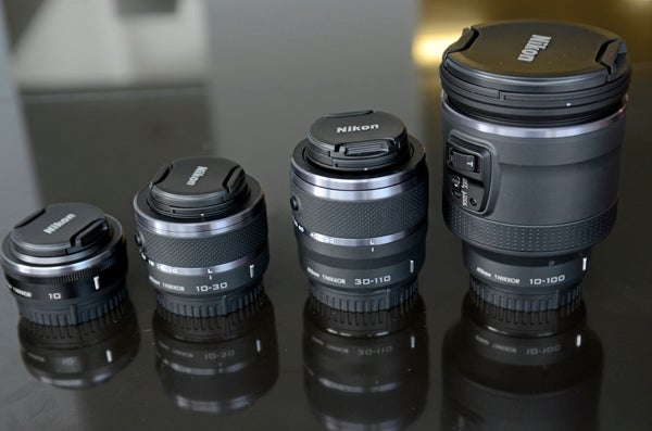 Nikon 1 5Assorted Nikon 1 lenses on reflective surface.